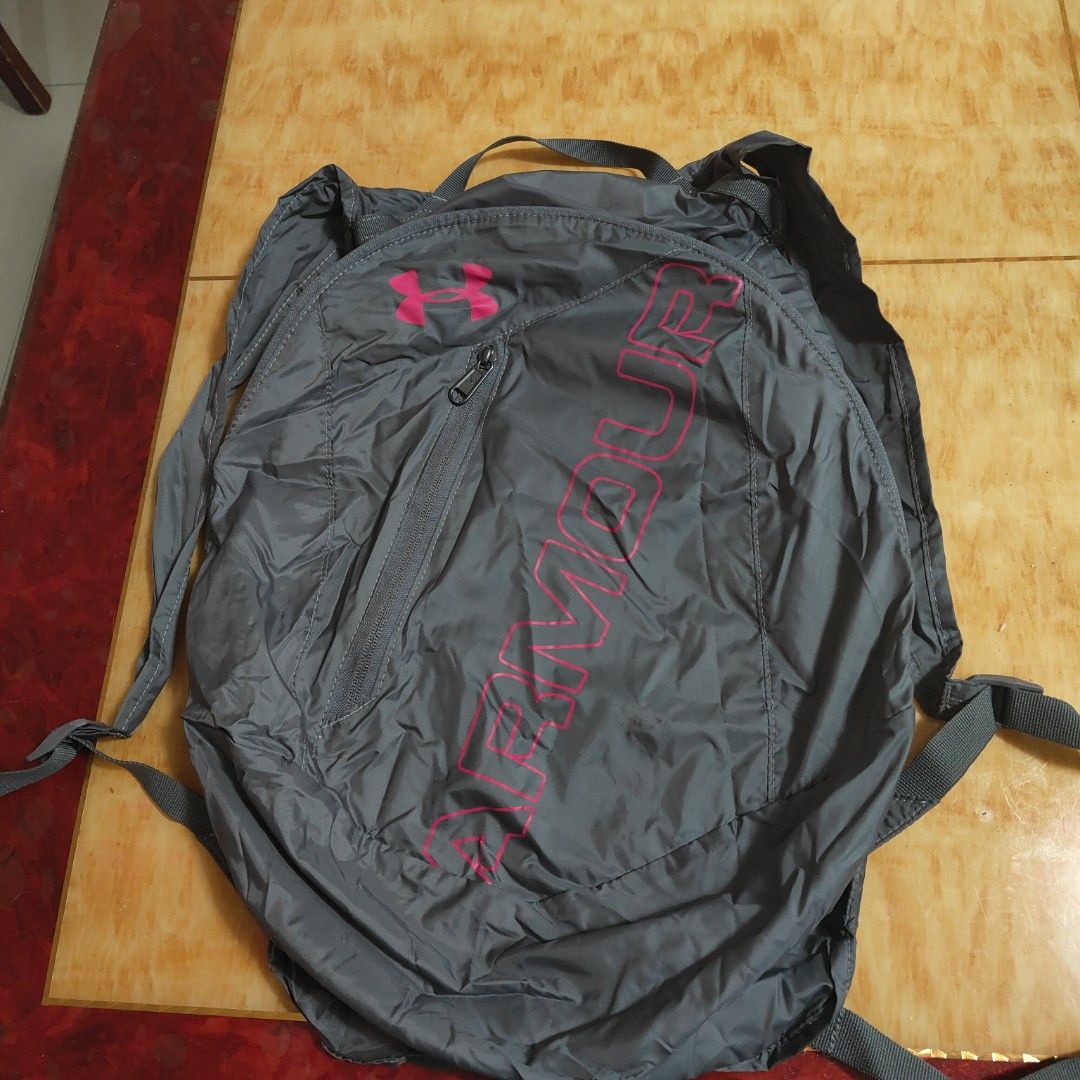Under Armour Foldable Backpack (Category: Backpacks) located in Valenzuela. Submitted by annamagabo (Listing ID 1435559531, Image 2). Description: - Under Armour foldable backpack - Gray exterior with pink accents - Zippered main compartment - Front zippered pocket - Adjustable straps - Top handle for easy carrying - Lightweight design - Under Armour logo displayed.