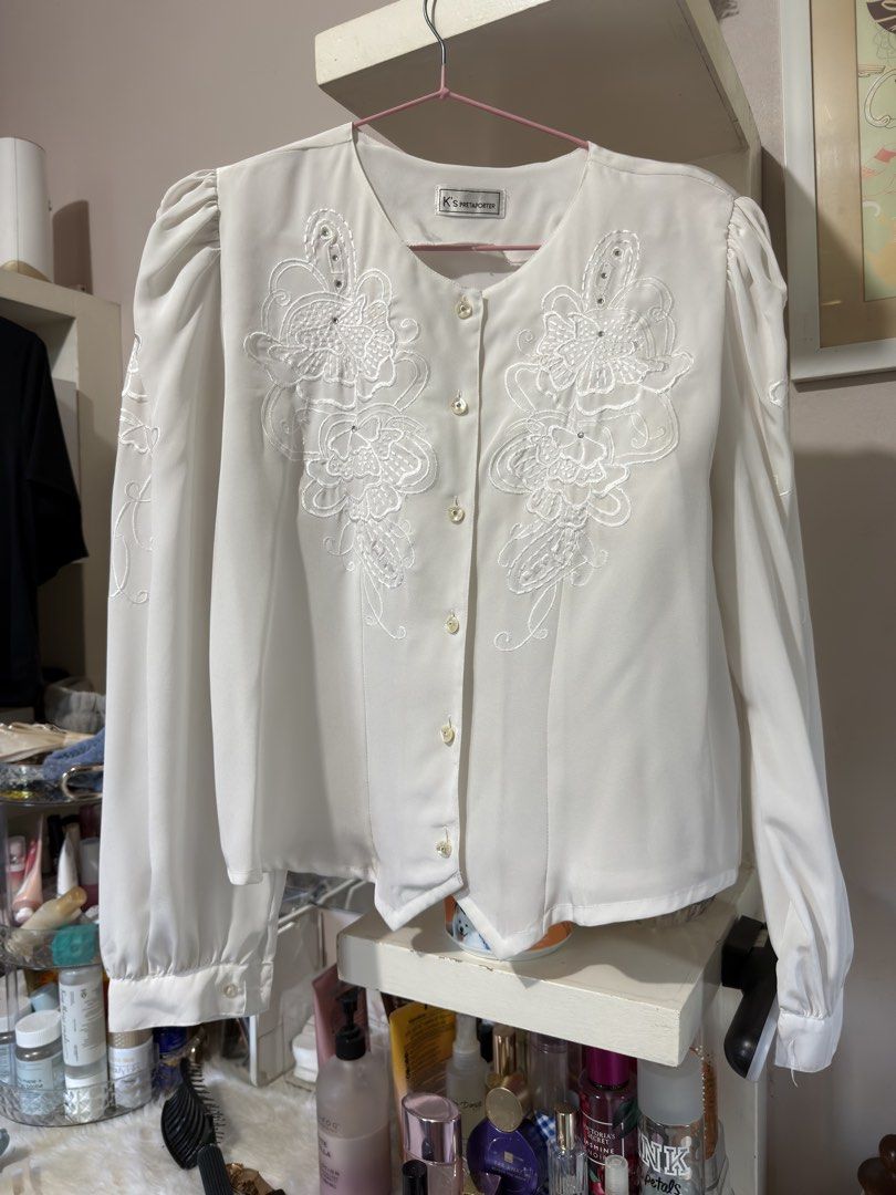Vintage White Embroidered Blouse (Category: Blouses) located in Apalit. Submitted by ic_declutter (Listing ID 1435606003, Image 1). Description: Elegant white blouse with intricate floral embroidery. Features a round neckline and button-down closure. The long sleeves have a slight puff at the shoulders. The blouse has a vintage aesthetic. The brand is K's International. A classic piece for any wardrobe..