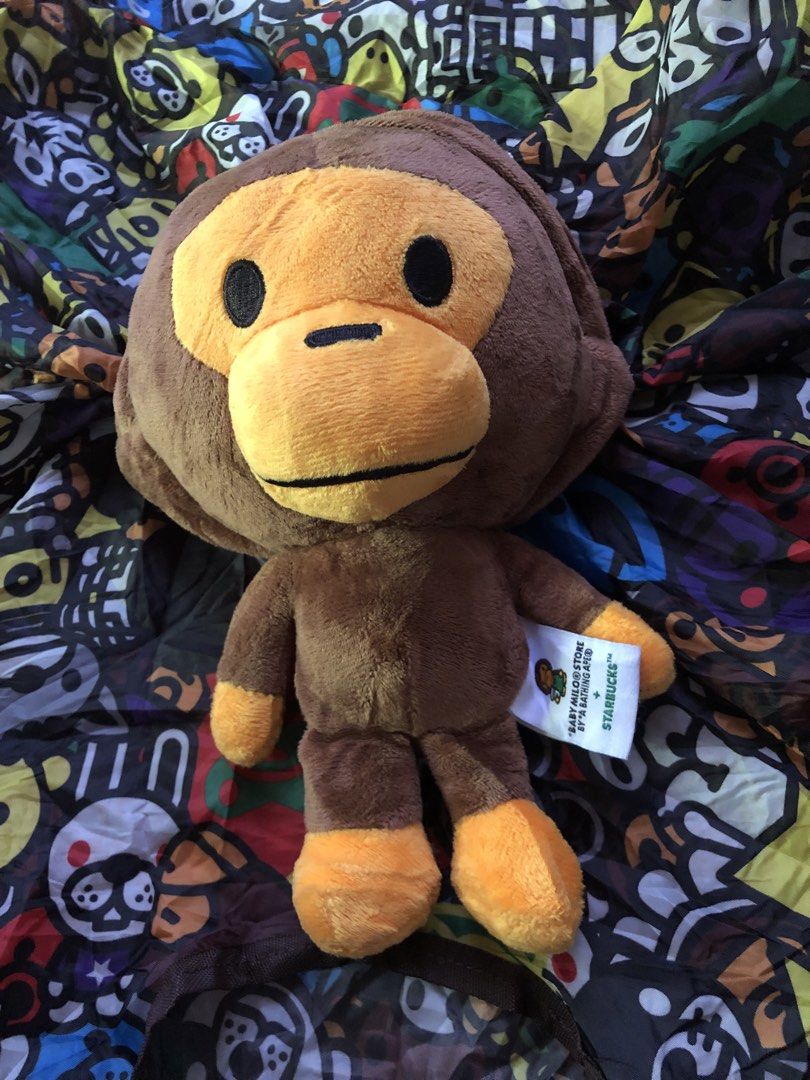 BAPE x Starbucks Monkey Plush Toy with Bag (Category: Plushies & Soft Toys) located in Montevista. Submitted by rdthriftshub (Listing ID 1438942130, Image 2). Description: - Authentic BAPE x Starbucks monkey plush toy - Comes with a matching patterned bag - Plush features a brown monkey with orange accents - Includes original tag - Bag features a colorful pattern - Plush toy can be stored inside the bag.