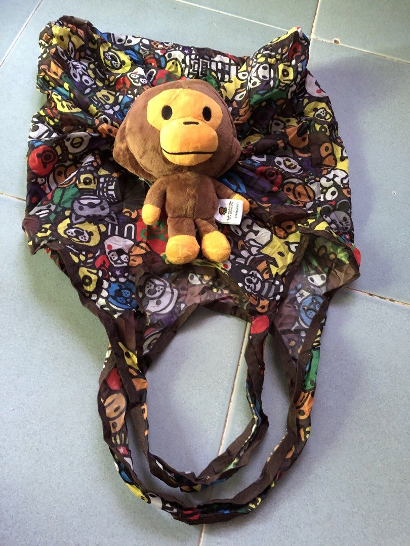 BAPE x Starbucks Monkey Plush Toy with Bag (Category: Plushies & Soft Toys) located in Montevista. Submitted by rdthriftshub (Listing ID 1438942130, Image 1). Description: - Authentic BAPE x Starbucks monkey plush toy - Comes with a matching patterned bag - Plush features a brown monkey with orange accents - Includes original tag - Bag features a colorful pattern - Plush toy can be stored inside the bag.