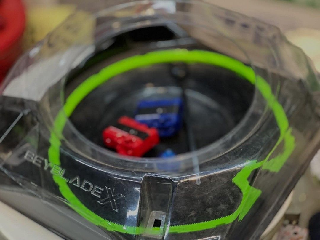 Beyblade X Stadium (Category: Action & Battle Toys) located in Valenzuela. Submitted by upcycle_things (Listing ID 1438960526, Image 3). Description: - Beyblade X stadium - Green accent ring - Black base - Clear plastic cover - Beyblade X logo visible - Includes blue and red Beyblade.