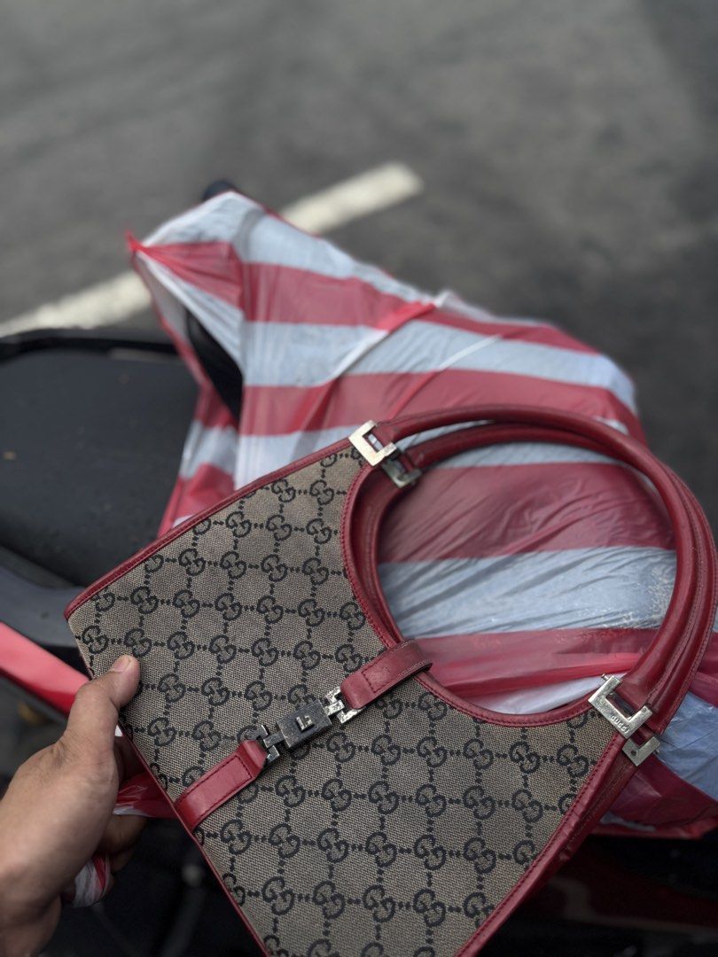 Gucci Handbag with Red Accents (Category: Luxury Bags & Wallets) located in Manila. Submitted by keantuttt (Listing ID 1438971004, Image 1). Description: - Gucci handbag - Iconic GG monogram pattern - Red leather straps and trim - Silver-tone buckle closure - 'Made in Italy' tag - Black fabric interior - Unique bag shape.