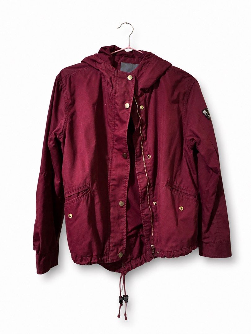 Maroon Hooded Jacket with Drawstring (Category: Coats, Jackets and Outerwear) located in Taguig. Submitted by julia_choose (Listing ID 1438926327, Image 1). Description: Maroon jacket with a hood and a drawstring at the hem. It features a zipper closure and snap buttons. There are two pockets on the front. The jacket has a small emblem on the sleeve. The jacket is hanging on a pink hanger..