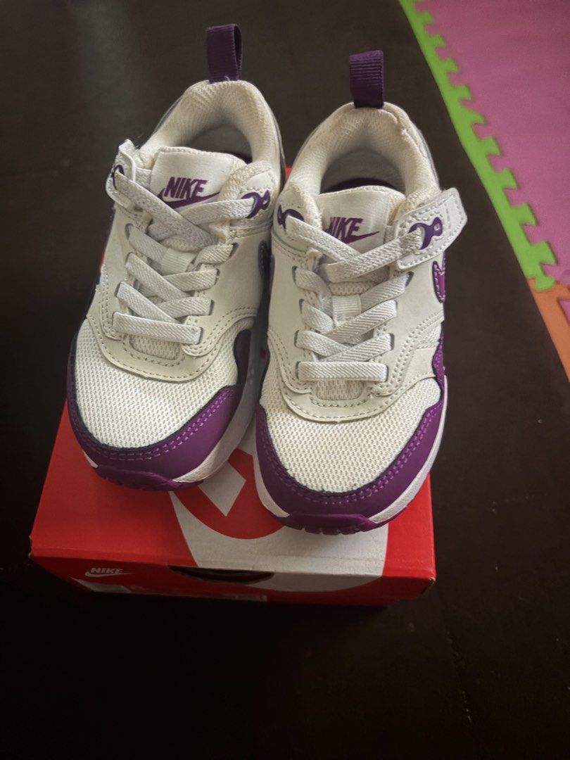 Nike Air Max 1 Easyon (PS) - 8C (Category: Babies & Kids Fashion) located in San Pedro. Submitted by AuthenticBrandedItems (Listing ID 1438968050, Image 1). Description: - Nike Air Max 1 Easyon (PS) sneakers - Color: White and Purple - Size: 8C - Easy-on design with hook-and-loop strap - Features Nike logo on side and tongue - Includes original box with Nike logo.