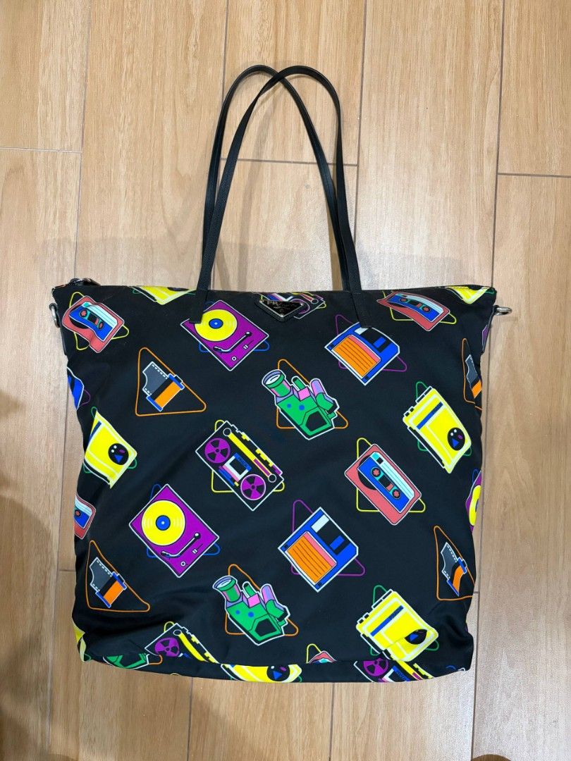 Prada Cassette Print Black Nylon Tote Bag (Category: Luxury Bags & Wallets) located in Mandaluyong City. Submitted by kimberlygo (Listing ID 1438897264, Image 1). Description: - Prada tote bag with cassette print design - Black leather handles - Secure zipper closure - Includes authenticity cards - Durable nylon exterior - Features retro cassette tapes and turntable images.