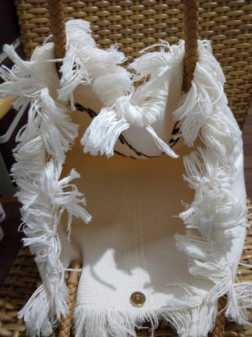 White Tote Bag with Braided Handles (Category: Tote Bags) located in Manila. Submitted by _bueta.09 (Listing ID 1438987377, Image 2). Description: - White fabric tote bag - Fringed top detail - Braided brown handles - Button closure - Light white interior - Suitable for carrying various items - Stylish and practical.