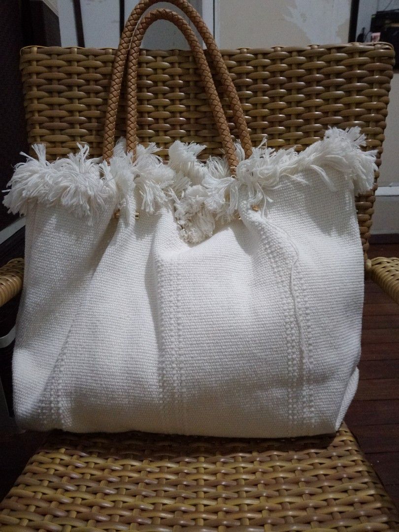 White Tote Bag with Braided Handles (Category: Tote Bags) located in Manila. Submitted by _bueta.09 (Listing ID 1438987377, Image 1). Description: - White fabric tote bag - Fringed top detail - Braided brown handles - Button closure - Light white interior - Suitable for carrying various items - Stylish and practical.