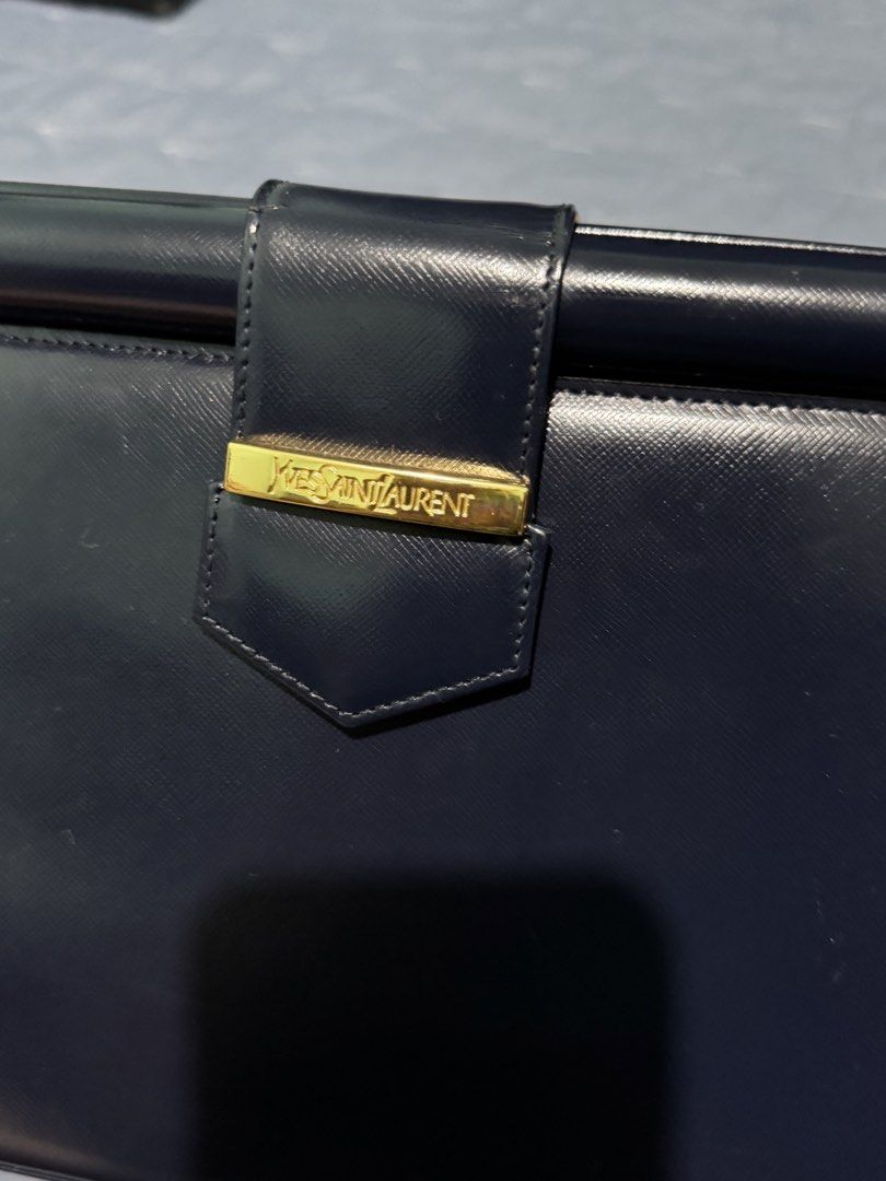Yves Saint Laurent Navy Clutch (Category: Luxury Bags & Wallets) located in Manila. Submitted by vera26 (Listing ID 1439015183, Image 3). Description: - Yves Saint Laurent navy clutch - Gold-tone clasp with YSL branding - Includes dust bag - Interior: Patterned lining with YSL logo - Shape: Rectangular - Closure: Flap - Exterior: Smooth material with minimal scratches.