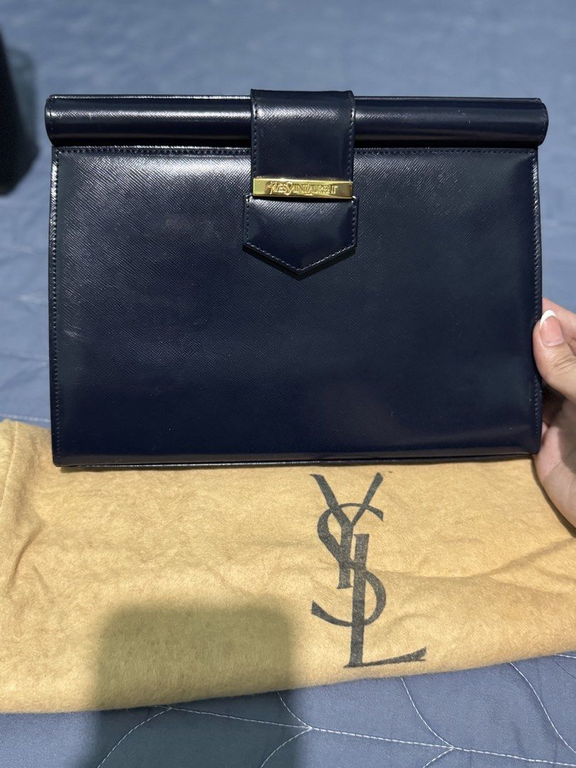 Yves Saint Laurent Navy Clutch (Category: Luxury Bags & Wallets) located in Manila. Submitted by vera26 (Listing ID 1439015183, Image 1). Description: - Yves Saint Laurent navy clutch - Gold-tone clasp with YSL branding - Includes dust bag - Interior: Patterned lining with YSL logo - Shape: Rectangular - Closure: Flap - Exterior: Smooth material with minimal scratches.