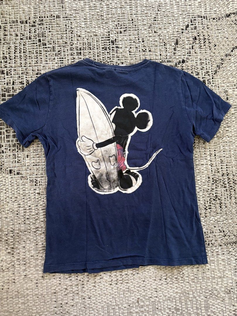 Zara Mickey Mouse Surf T-shirt (Category: Tshirts & Polo Shirts ) located in Binan City. Submitted by morticias_vault (Listing ID 1439107225, Image 2). Description: - Zara navy blue t-shirt - Features a Mickey Mouse surfing graphic (front and back) - Crew neck and short sleeves - Size: S (fits kids aged 12) - Made in Portugal Color may vary due to lighting.