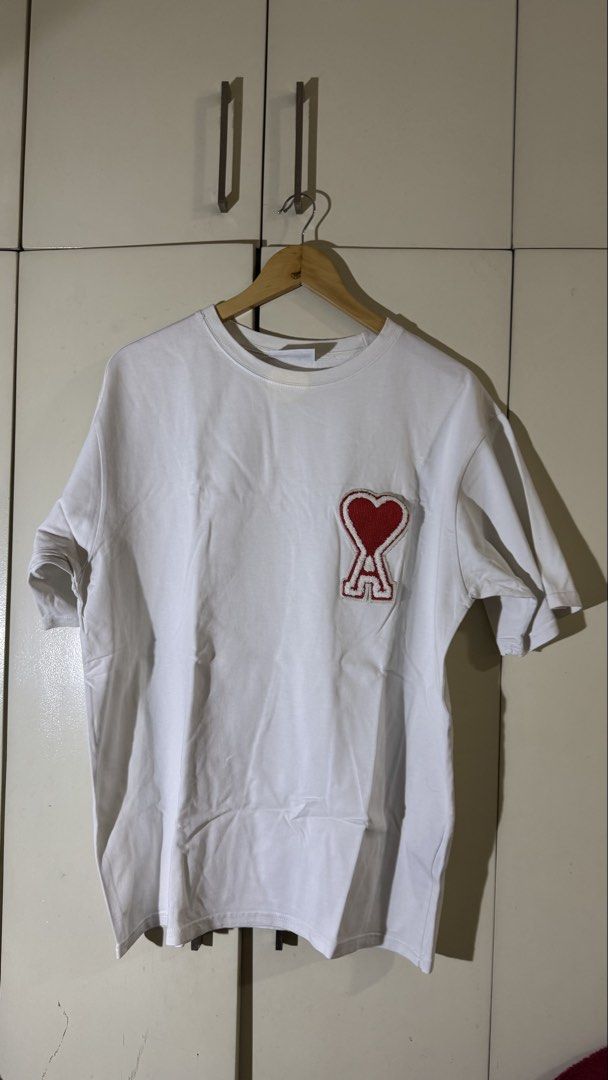 AMI Paris Heart Logo T-shirt (Category: Tshirts & Polo Shirts ) located in Quezon City. Submitted by mogsmogs (Listing ID 1439391864, Image 1). Description: - AMI Paris T-shirt - Features the iconic red heart logo - Crew neck design - Short sleeves - Made in Portugal Washable stain Dimes: 22 width x 27 length Rfs: nakatambak sa closet, tumaba ako.