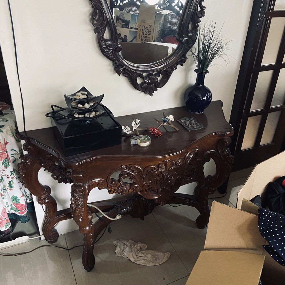 Vintage Carved Console Table with Mirror (Category: Tables & Sets) located in Paranaque City. Submitted by furniture_seller_jay (Listing ID 1439269923, Image 1). Description: Elegant antique console table with intricate carvings. Features a dark wood finish and a matching ornate mirror. The table has a curved design with detailed floral patterns. Includes a dark blue vase and decorative items on top. Perfect for entryways or living rooms. The mir