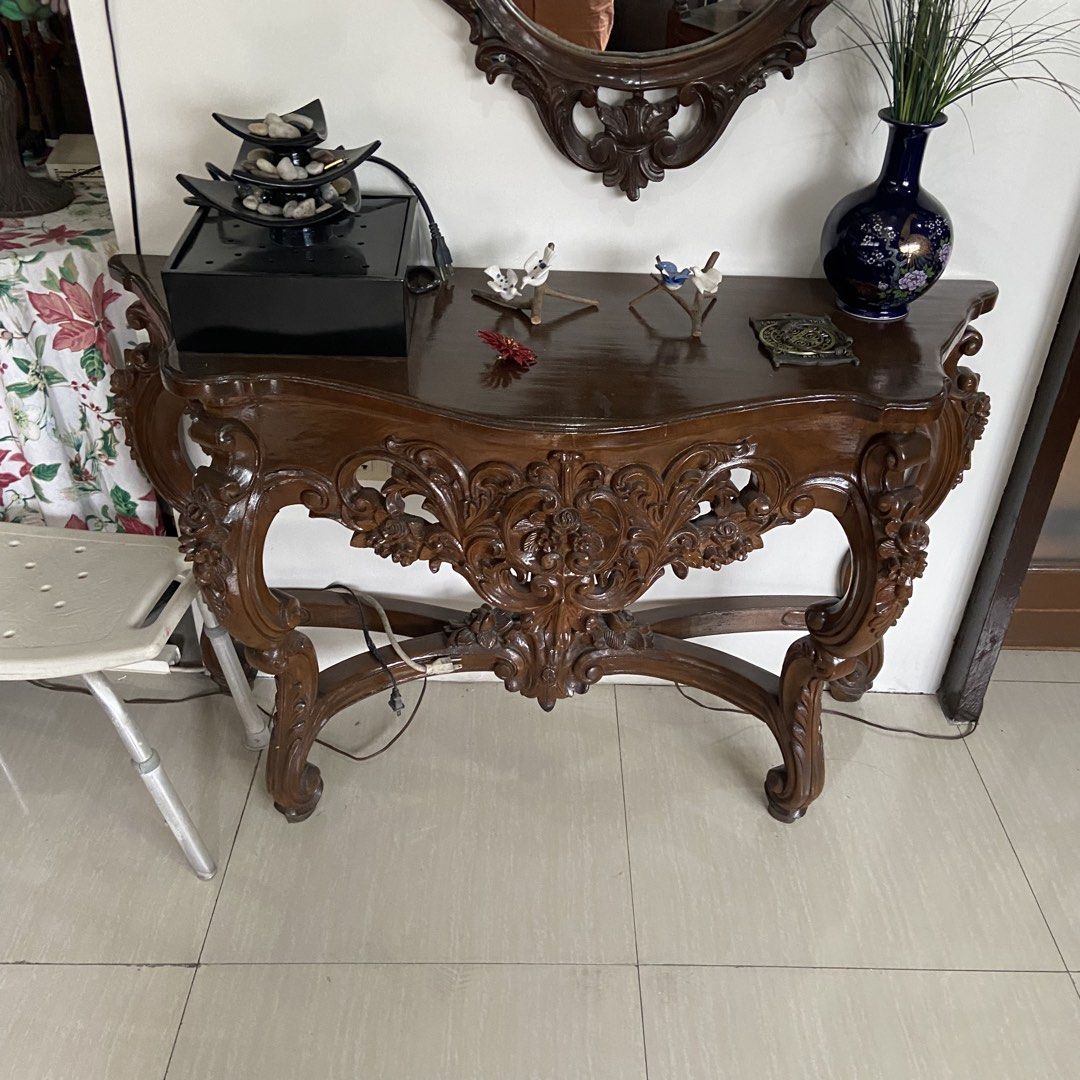 Vintage Carved Console Table with Mirror (Category: Tables & Sets) located in Paranaque City. Submitted by furniture_seller_jay (Listing ID 1439269923, Image 3). Description: Elegant antique console table with intricate carvings. Features a dark wood finish and a matching ornate mirror. The table has a curved design with detailed floral patterns. Includes a dark blue vase and decorative items on top. Perfect for entryways or living rooms. The mir