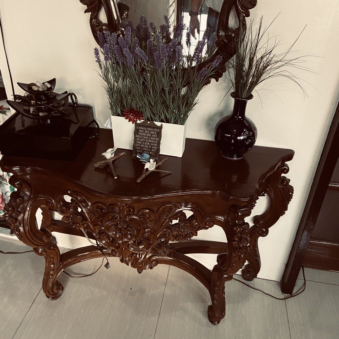 Vintage Carved Console Table with Mirror (Category: Tables & Sets) located in Paranaque City. Submitted by furniture_seller_jay (Listing ID 1439269923, Image 2). Description: Elegant antique console table with intricate carvings. Features a dark wood finish and a matching ornate mirror. The table has a curved design with detailed floral patterns. Includes a dark blue vase and decorative items on top. Perfect for entryways or living rooms. The mir