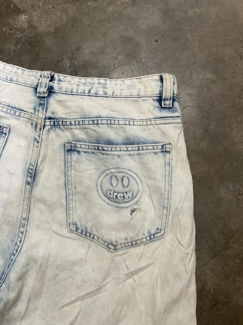 Drew House Acid Wash Jeans (Category: Jeans) located in Manila. Submitted by teampuyat224792 (Listing ID 1439376631, Image 3). Description: - Drew House acid wash jeans - Light blue wash - Relaxed fit - Smiley face logo on back pocket - Drew House branding on waistband - Button fly closure - Minor tear on front - waistline 34 - thigh 13.5 - length 39.5 - hem 8 .