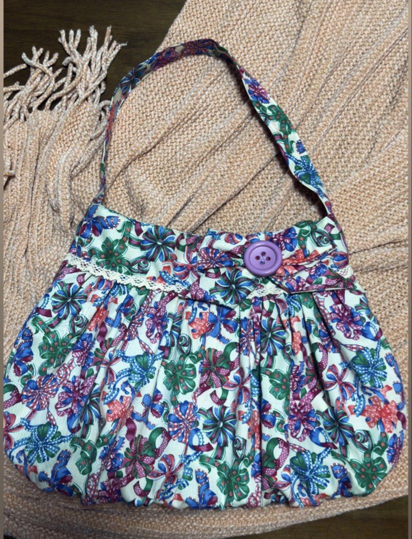 Floral Fabric Handbag with Purple Button (Category: Tote Bags) located in Angeles City. Submitted by delle_25 (Listing ID 1439348157, Image 1). Description: - Adorable floral patterned handbag - Features a white base - Rounded shape with a handle - Decorative lace trim - Secured with a large purple button - Made of cotton or similar fabric - Unique and stylish accessory.