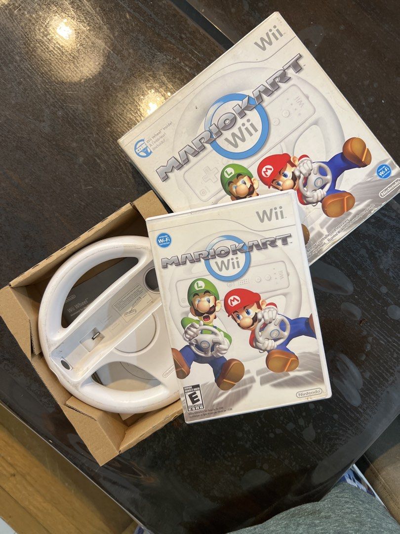 Mario Kart Wii with Steering Wheel (Category: Nintendo) located in Bacoor. Submitted by homergarage (Listing ID 1439298966, Image 1). Description: - Mario Kart Wii game for Nintendo Wii. - Includes game disc. - Comes with a white steering wheel accessory. - Features Mario and Luigi on the cover. - Box and steering wheel are white..