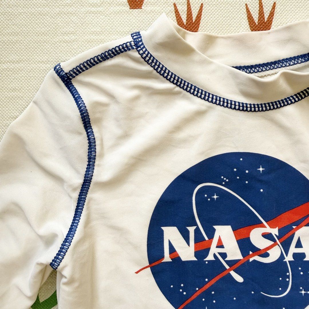 NASA Long Sleeve Rash Guard (Category: Babies & Kids Fashion) located in Davao. Submitted by taycodissimo_apparel (Listing ID 1439263895, Image 2). Description: - White long-sleeved rash guard - Features a NASA logo - Blue stitching details - Designed for sun protection - Perfect for water activities - Suitable for children.
