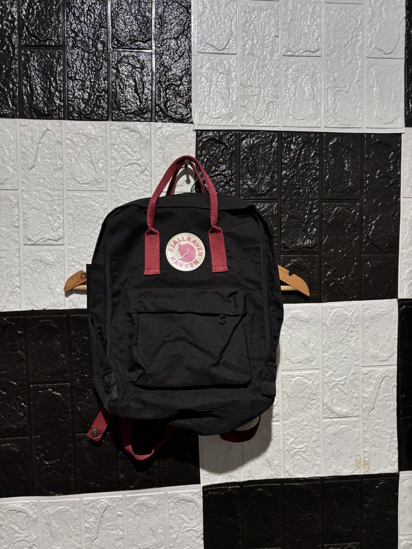 Fjallraven Kanken Backpack (Category: Backpacks) located in Lopez. Submitted by thrift.ni.roms22 (Listing ID 1439559793, Image 1). Description: Black Fjallraven Kanken backpack with red straps. Features a front pocket and a main compartment with a zipper closure. The Fjallraven logo is visible on the front. Includes adjustable shoulder straps and a top handle. The backpack has a classic design..