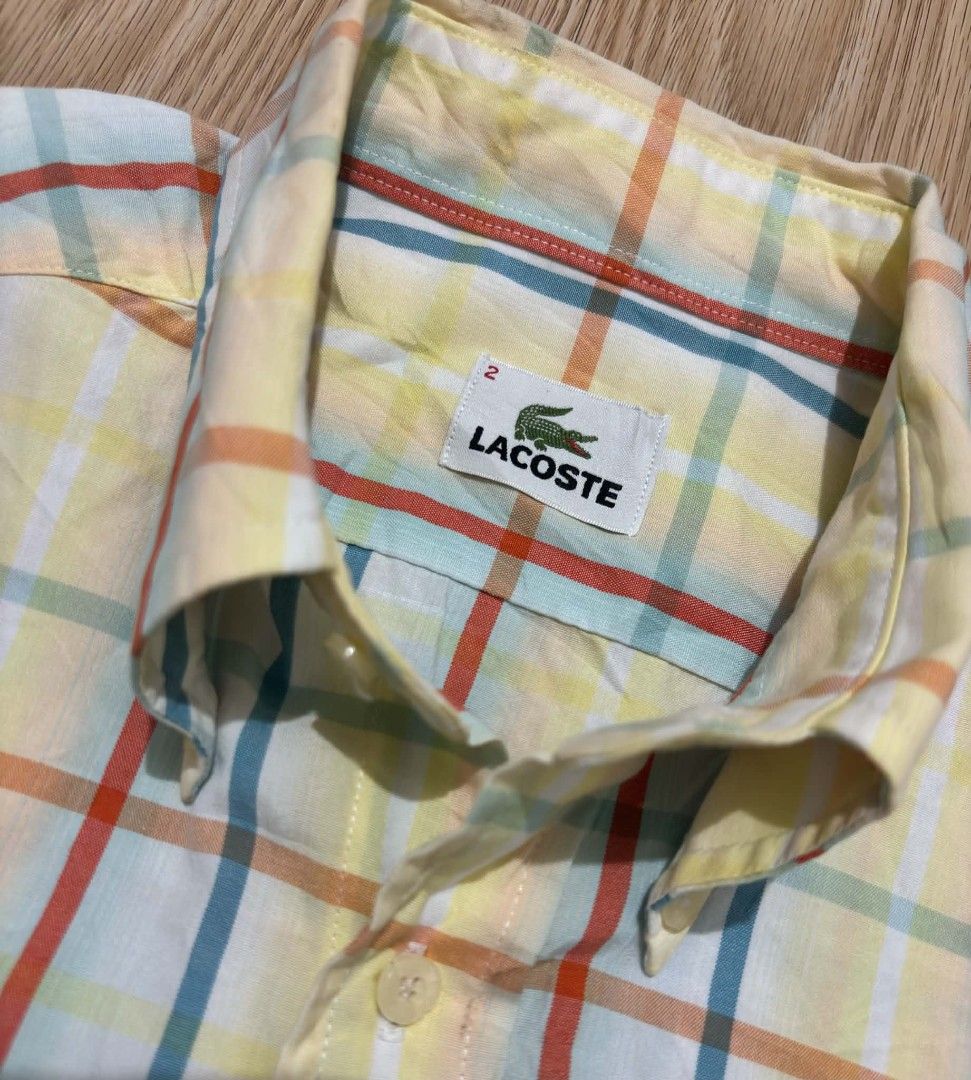 Lacoste Plaid Short Sleeve Shirt (Category: Tshirts & Polo Shirts ) located in Alegria. Submitted by gems07 (Listing ID 1439555610, Image 2). Description: - Lacoste short sleeve shirt - Size 2 - Plaid pattern (yellow base with blue, red, and orange lines) - Button-down collar - Chest pocket with Lacoste logo - Made in Japan -length 26 n half / width 19.