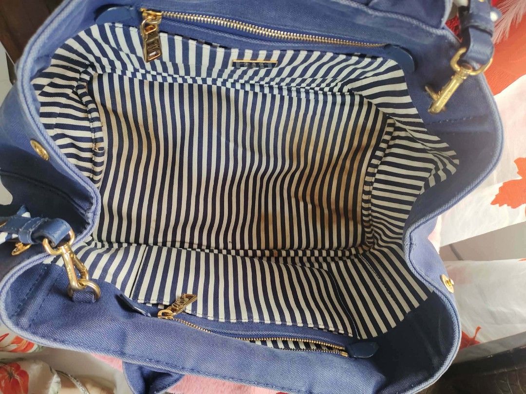 Prada Canvas Tote Bag denim canvass(dirt lining) (Category: Luxury Bags & Wallets) located in Cebu City. Submitted by tlisurplus (Listing ID 1439511899, Image 2). Description: - Authentic Prada tote bag - Blue canvas material - Striped interior lining - Detachable shoulder strap - Gold-tone hardware - Top handle - Zipper closure - Prada logo on front - Interior pocket with Prada label.