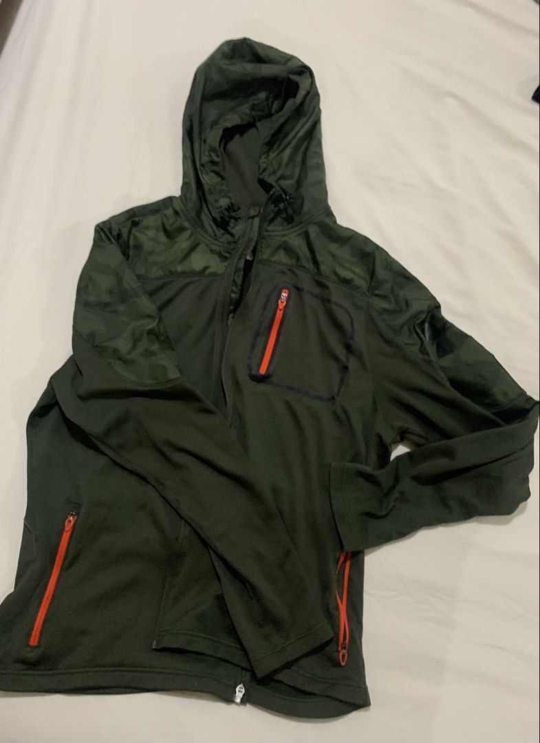 Under Armour Green Camo Hooded Jacket (Category: Coats, Jackets and Outerwear) located in Paranaque City. Submitted by vbvessentials (Listing ID 1439560981, Image 2). Description: Under Armour jacket features a green color with camo detailing on the hood and shoulders. It has a zip-up front, two side pockets, and a chest pocket, all with orange zippers. The jacket includes a hood with adjustable drawstrings. The size is Large. Flaw: the pull tab 