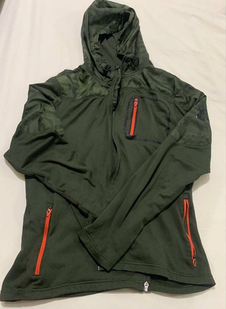 Under Armour Green Camo Hooded Jacket (Category: Coats, Jackets and Outerwear) located in Paranaque City. Submitted by vbvessentials (Listing ID 1439560981, Image 1). Description: Under Armour jacket features a green color with camo detailing on the hood and shoulders. It has a zip-up front, two side pockets, and a chest pocket, all with orange zippers. The jacket includes a hood with adjustable drawstrings. The size is Large. Flaw: the pull tab 
