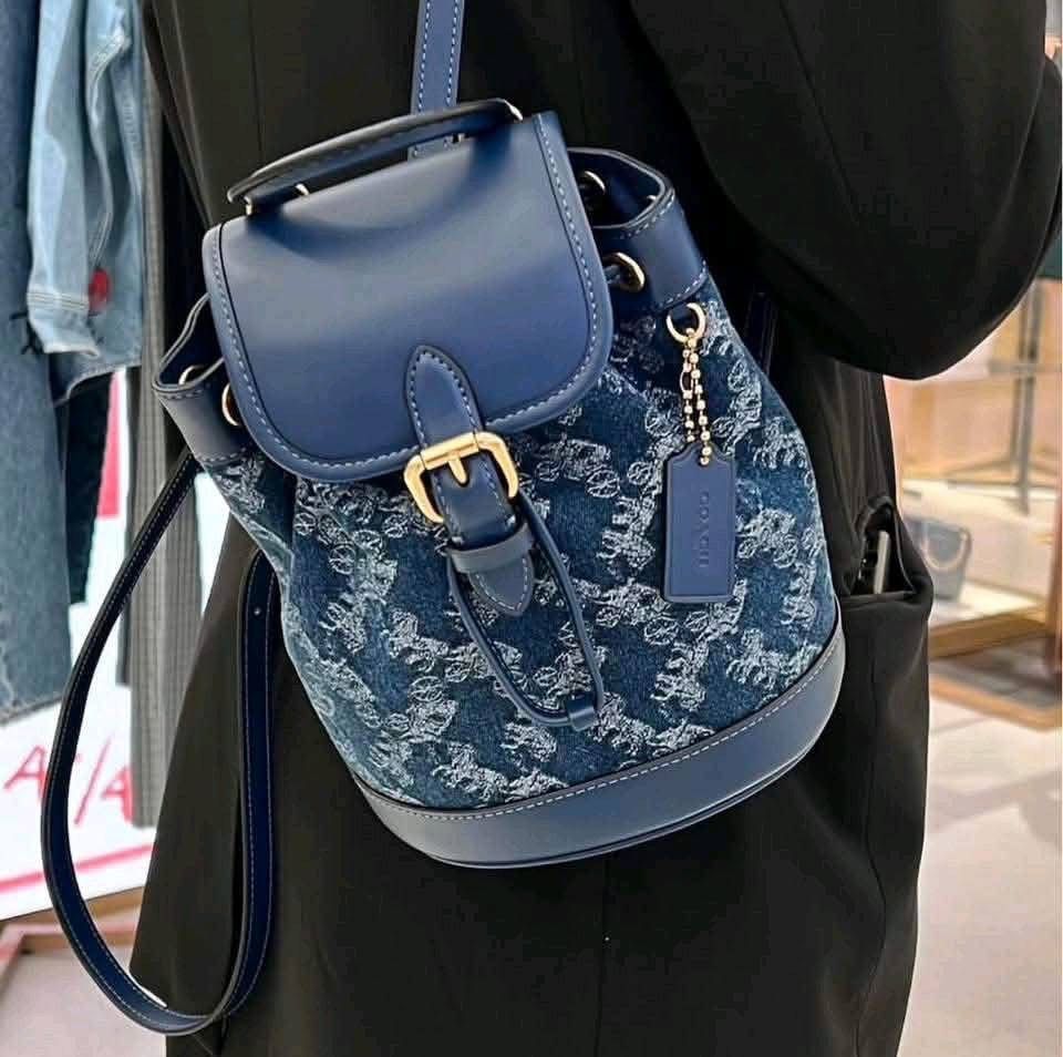 Coach Denim Backpack (Category: Backpacks) located in Manila. Submitted by arwanka29 (Listing ID 1439783780, Image 1). Description: Coach backpack features a denim exterior with a horse and carriage pattern. It has a flap closure with a buckle and a drawstring closure. The backpack has a top handle and adjustable shoulder straps. The interior is lined and includes a small pocket. The bag is made in Cambodia..