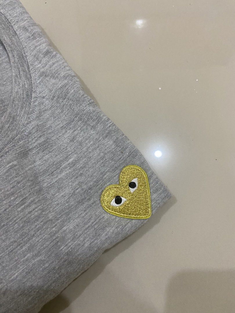 Comme des Garcons Play T-shirt (Category: Shirts) located in Lapu Lapu. Submitted by trip-thrift (Listing ID 1439752920, Image 3). Description: - Gray Comme des Garcons Play t-shirt - Features iconic yellow heart logo - Size: M - Classic crew neck and short sleeves - Authentic brand tag inside collar - Small logo detail on sleeve.