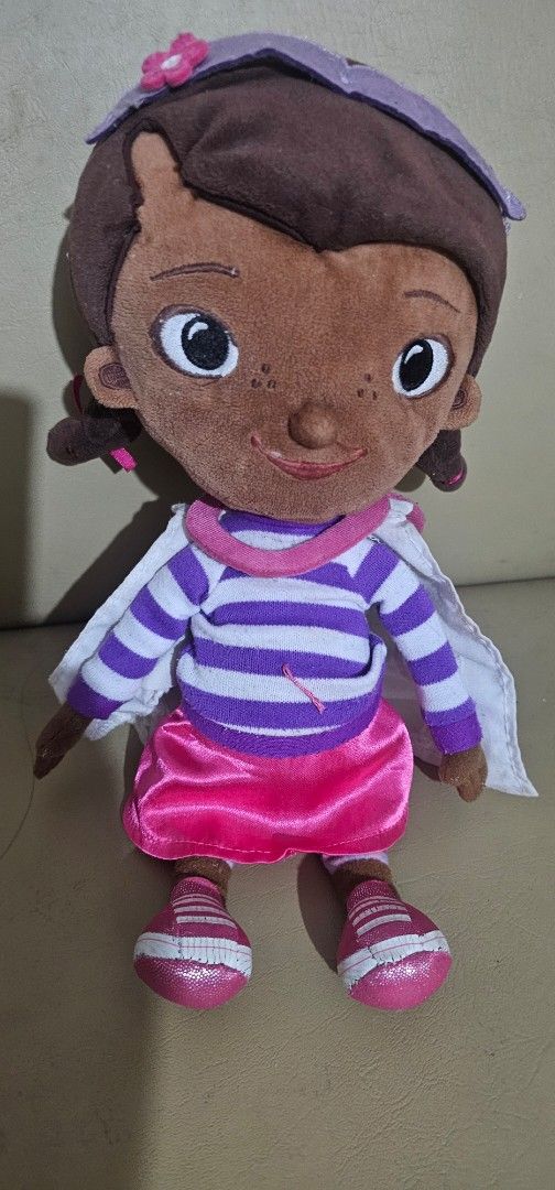 Doc McStuffins Plush Doll (Category: Plushies & Soft Toys) located in Cainta. Submitted by cyjozuza (Listing ID 1439770845, Image 1). Description: - Doc McStuffins plush doll - Brown face with freckles - Purple head covering with pink flower - White and purple striped shirt - Pink skirt - Pink shoes with white stripes - White cape - Pink collar.