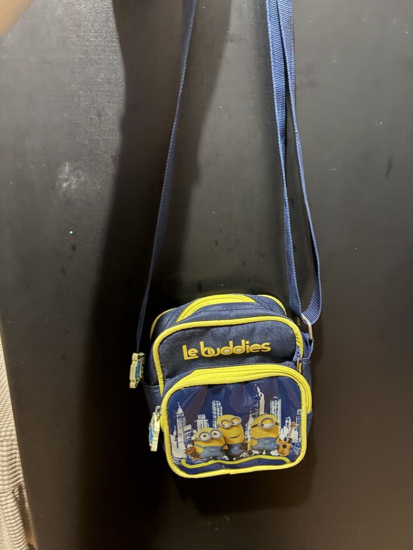 Le Buddies Minions Crossbody Bag (Category: Cross-body Bags) located in Quezon City. Submitted by grai25 (Listing ID 1439676355, Image 2). Description: - Le Buddies Minions Crossbody Bag - Fun Minions design - Main compartment with zipper - Front pocket with zipper - Blue strap - Yellow trim - Features "Le Buddies" text and Minions against a city skyline.