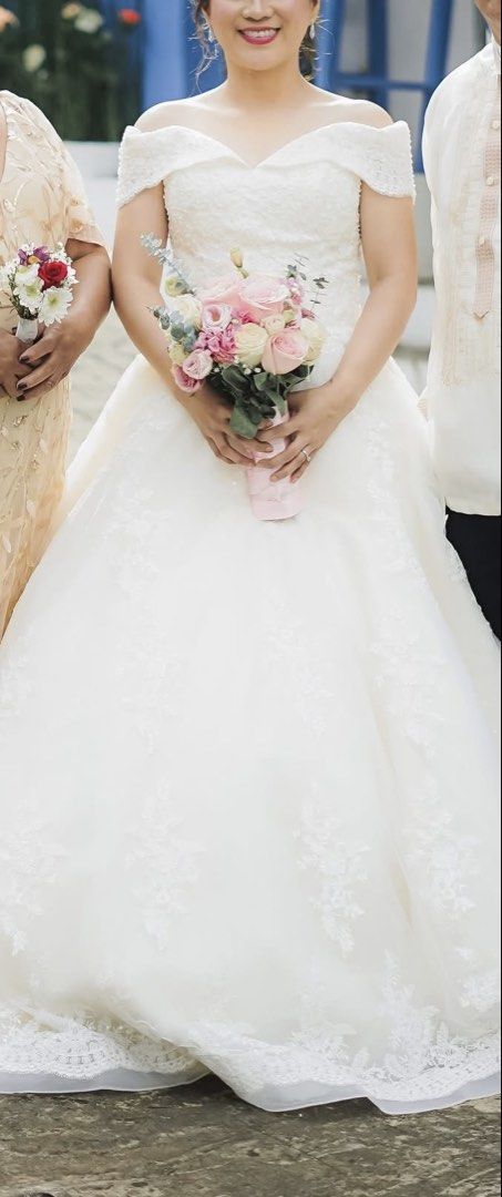 Off-Shoulder Ball Gown Wedding Dress (Category: Evening dresses & gowns) located in Legazpi City. Submitted by mblangcauon (Listing ID 1439657976, Image 2). Description: - Off-shoulder ball gown wedding dress - Features intricate lace detailing on bodice and skirt - Flowing, full skirt with lace trim - Color: White - Ideal for special occasions.