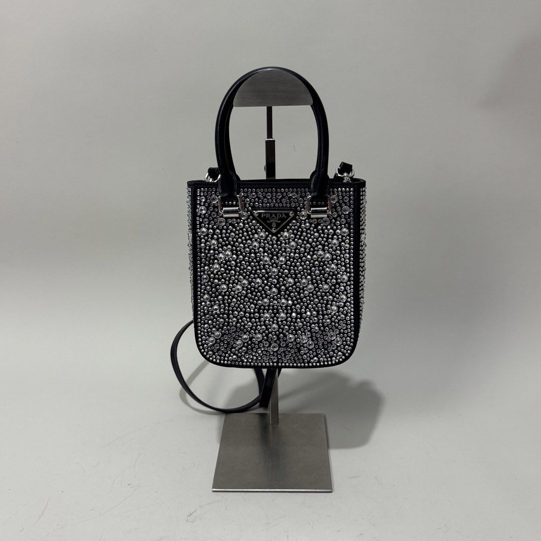 Prada Mini Handbag with Embellishments (Category: Luxury Bags & Wallets) located in Dagupan City. Submitted by thriftygoods.dagupan (Listing ID 1439609323, Image 1). Description: Prada mini handbag features a black leather exterior fully embellished with silver-toned studs. It has a top handle and a detachable shoulder strap. The interior includes a Prada logo plaque. Made in Italy..