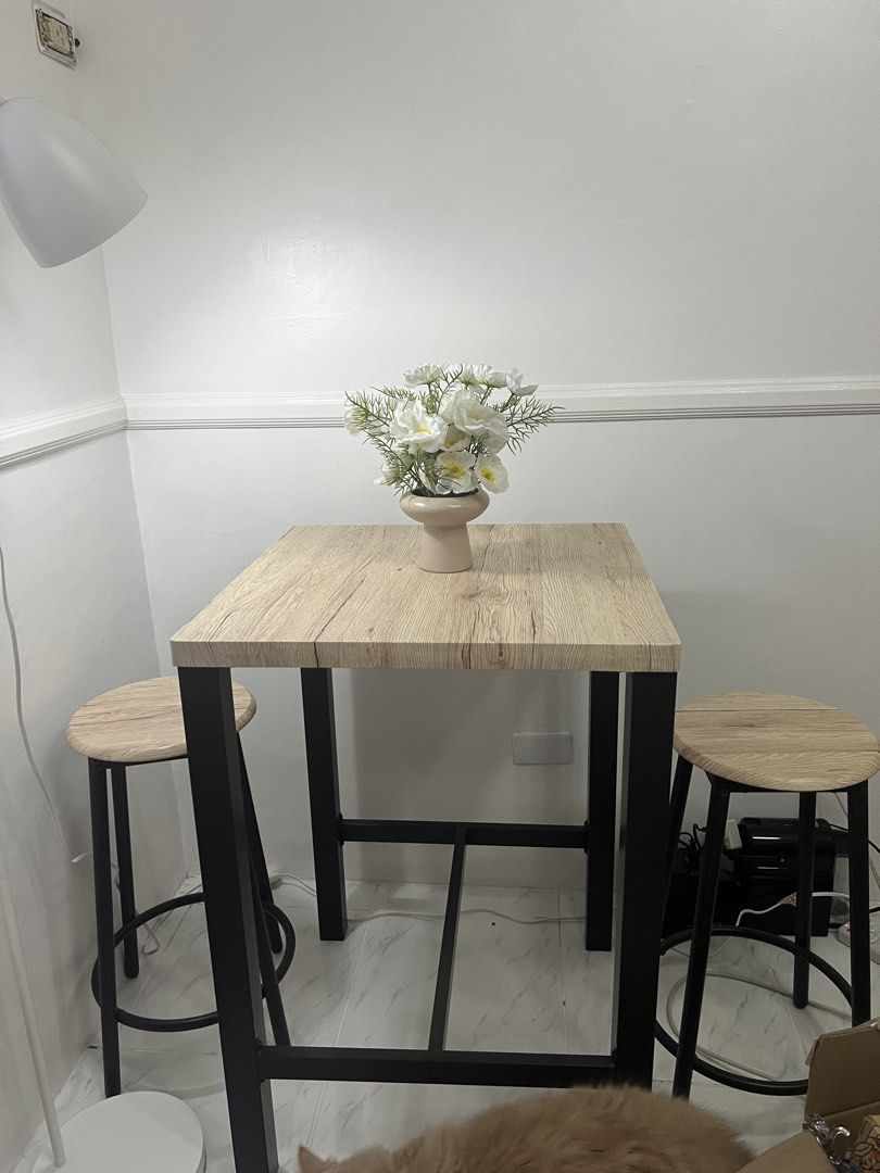 Square Table with Two Stools (Category: Tables & Sets) located in Paranaque City. Submitted by prelovers.ph (Listing ID 1439715273, Image 2). Description: Set includes a square table and two stools. The table has a light wood-grain finish and black metal legs. The stools have matching light wood-grain seats and black metal legs. Perfect for a small dining area or a breakfast nook. The set is compact and stylish. **Vase not included.