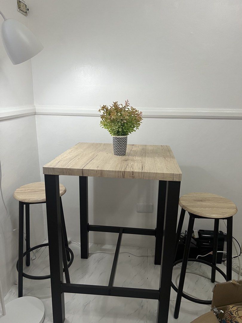 Square Table with Two Stools (Category: Tables & Sets) located in Paranaque City. Submitted by prelovers.ph (Listing ID 1439715273, Image 1). Description: Set includes a square table and two stools. The table has a light wood-grain finish and black metal legs. The stools have matching light wood-grain seats and black metal legs. Perfect for a small dining area or a breakfast nook. The set is compact and stylish. **Vase not included.