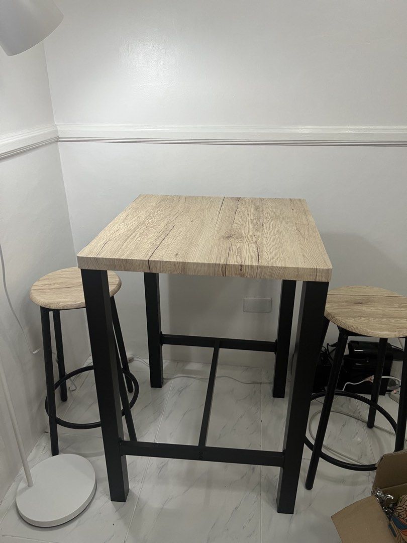 Square Table with Two Stools (Category: Tables & Sets) located in Paranaque City. Submitted by prelovers.ph (Listing ID 1439715273, Image 3). Description: Set includes a square table and two stools. The table has a light wood-grain finish and black metal legs. The stools have matching light wood-grain seats and black metal legs. Perfect for a small dining area or a breakfast nook. The set is compact and stylish. **Vase not included.