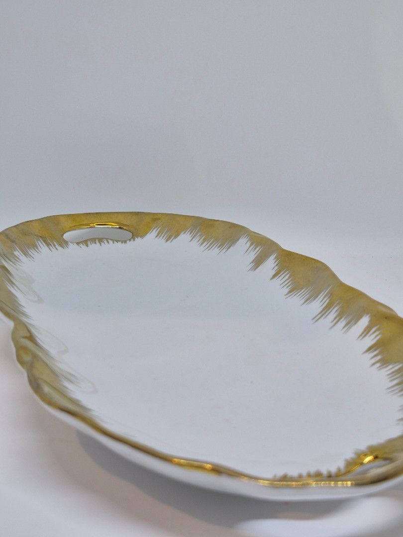Vintage White and Gold Serving Tray (Category: Dinnerware & Cutlery) located in Santa Rosa. Submitted by thesecondshelf (Listing ID 1439747938, Image 1). Description: Vintage White and Gold Serving Tray ₱550 Details: • Vintage ceramic serving tray • White glazed surface with hand-painted gold border • Elegant scalloped form with open handles • Classic display and serving piece • Approx. 32–34 cm length Condition: Good vintage condition with age-a