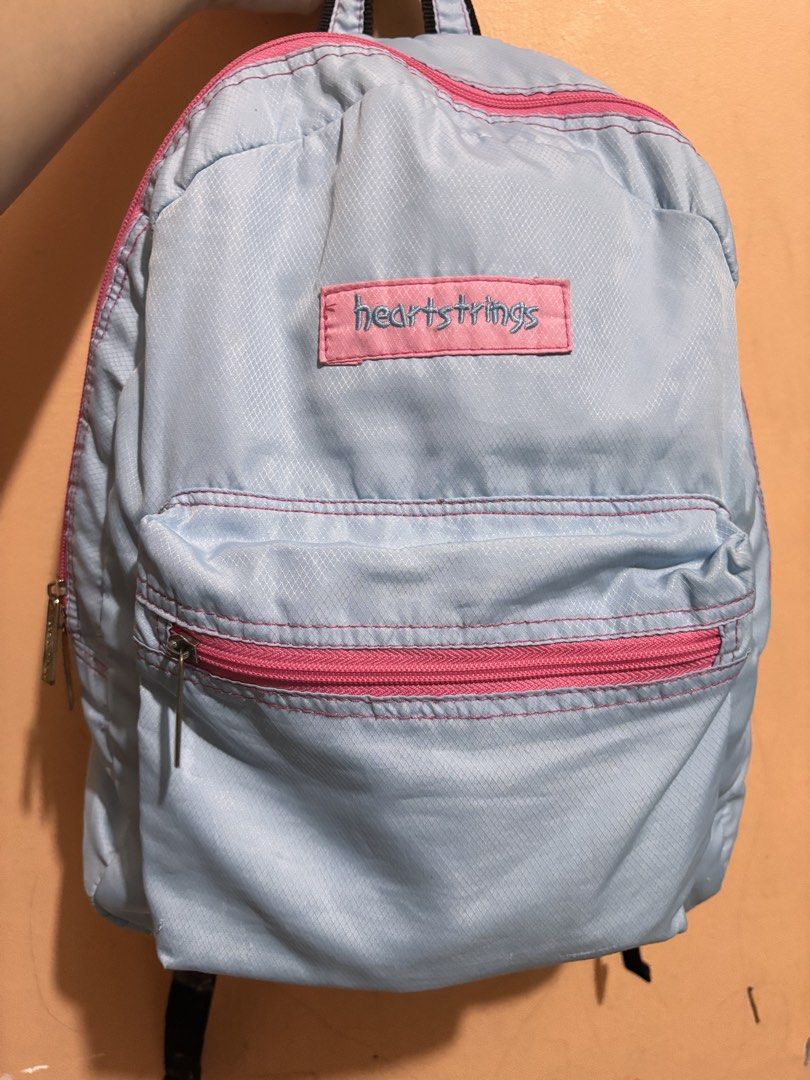 Heartstrings Blue Backpack (Category: Backpacks) located in San Fernando. Submitted by ladychinita07 (Listing ID 1439814959, Image 1). Description: - Light blue Heartstrings backpack - Pink zippers and stitching - Front pocket - Adjustable straps - Brand name on front - Brand name engraved on zippers - Straps show wear.