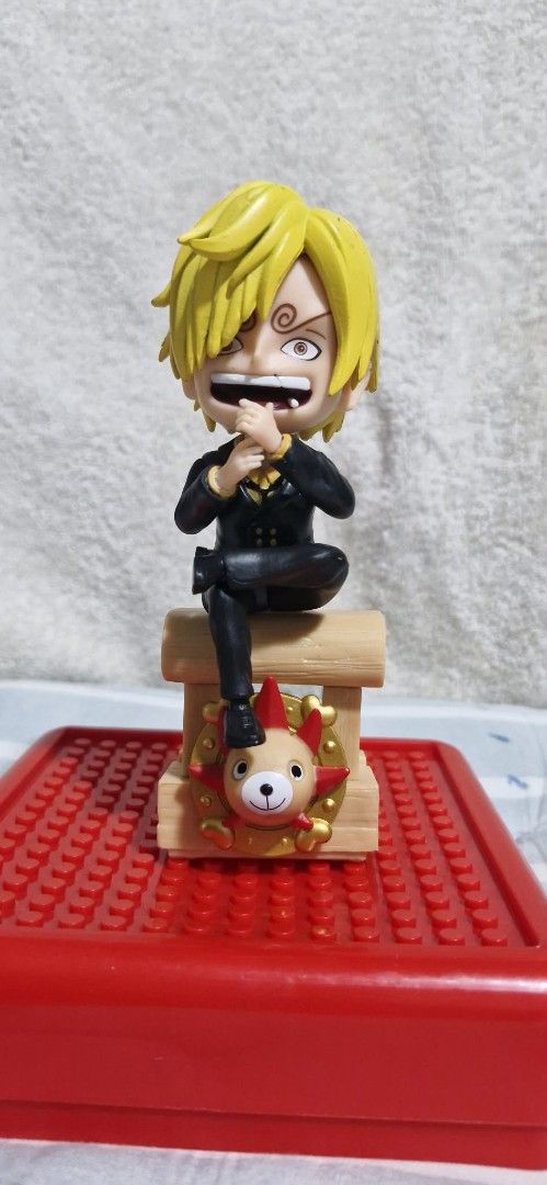 One Piece Sanji Chibi Figure with Stand (Category: Figurines & Statues) located in Paranaque City. Submitted by licadoodles (Listing ID 1439935783, Image 1). Description: - Adorable Sanji chibi figure from One Piece - Features his iconic blonde hair and determined expression - Comes with a wooden stand - Stand has a red and gold emblem with a bear-like character - Perfect collectible for any One Piece enthusiast.