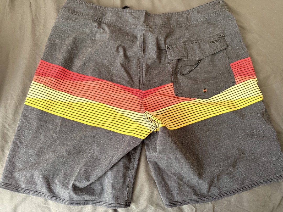 Quiksilver Board Shorts - Size 34 (Category: Swim Trunks & Board Shorts) located in Quezon City. Submitted by wringwraith (Listing ID 1439825241, Image 2). Description: Quiksilver board shorts in size 34. Features a gray base with a horizontal stripe design in red, orange, and yellow. Includes a back pocket and a drawstring closure. The shorts have a Quiksilver logo patch. Made with 4-way stretch material. Condition: 8/10 Size 34 on tag Issues: F