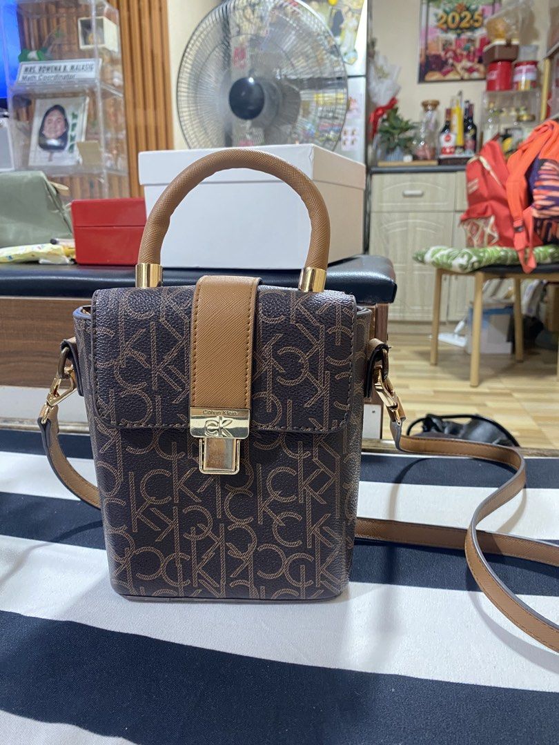Calvin Klein Monogram Box Bag with Strap (Category: Luxury Bags & Wallets) located in Bulacan. Submitted by pmlsg (Listing ID 1440033410, Image 2). Description: - Stylish Calvin Klein box bag - Signature monogram print - Top handle - Detachable crossbody strap for versatile carrying - Lined interior with compartments - Secure gold-tone clasp closure.