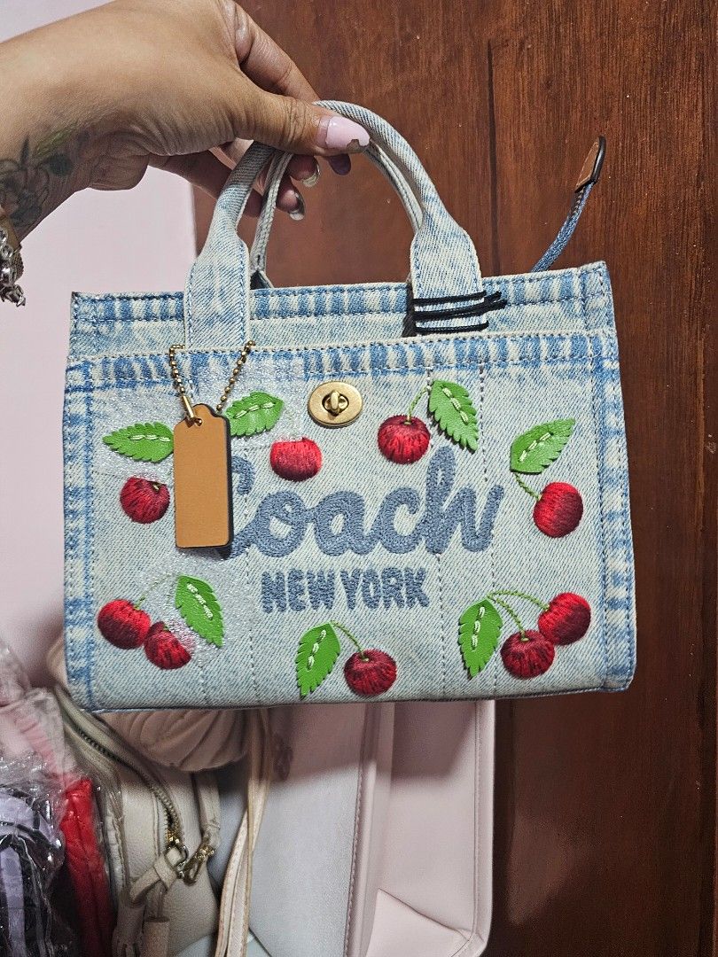 Coach New York Denim Cherry Mini Tote Bag (Category: Luxury Bags & Wallets) located in Angeles City. Submitted by kodachi10 (Listing ID 1440151713, Image 1). Description: - Authentic Coach New York mini tote bag - Light wash denim material - Charming all-over embroidered cherry motif - Secure turn-lock closure - Detachable leather hangtag - Perfect for adding a fun pop to your outfit - Bought in the US at retail price - Comes with sling.