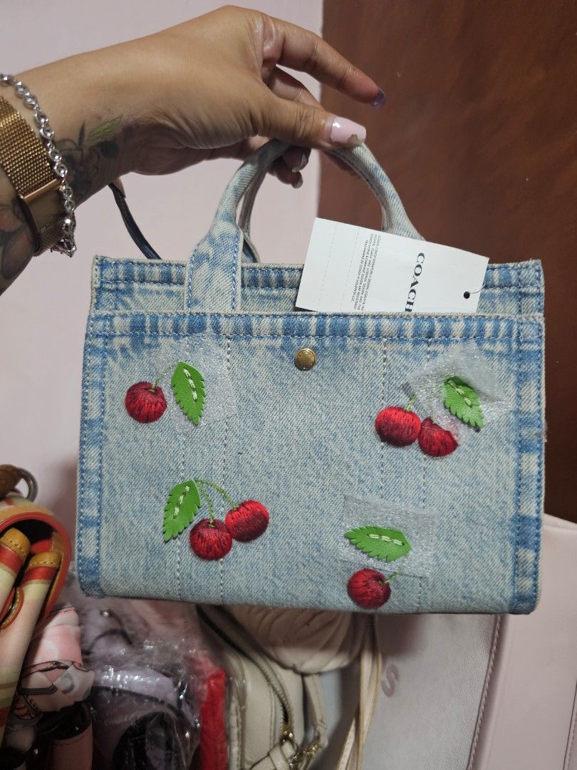 Coach New York Denim Cherry Mini Tote Bag (Category: Luxury Bags & Wallets) located in Angeles City. Submitted by kodachi10 (Listing ID 1440151713, Image 2). Description: - Authentic Coach New York mini tote bag - Light wash denim material - Charming all-over embroidered cherry motif - Secure turn-lock closure - Detachable leather hangtag - Perfect for adding a fun pop to your outfit - Bought in the US at retail price - Comes with sling.