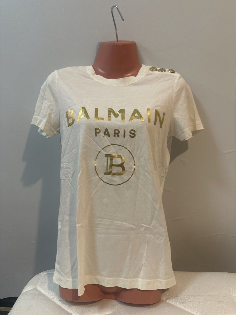 Balmain Paris White T-shirt (Category: Shirts) located in Las Pinas. Submitted by Mkdot (Listing ID 1439832044, Image 1). Description: - Balmain Paris T-shirt - White with gold print - Crew neck - Short sleeves - Decorative gold buttons on shoulder - Plain white back - Lightweight fabric.
