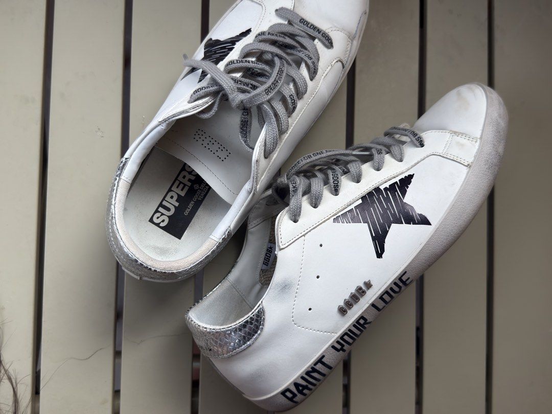 Golden Goose Superstar Sneakers (Category: Sneakers) located in Cavite. Submitted by ranmii77 (Listing ID 1439263369, Image 3). Description: Golden Goose Superstar sneakers in white with a black star design. Features grey laces with "Golden Goose" text. The heel has a snakeskin pattern. The insole has the "SUPERSTAR" logo. The shoes have a distressed look..