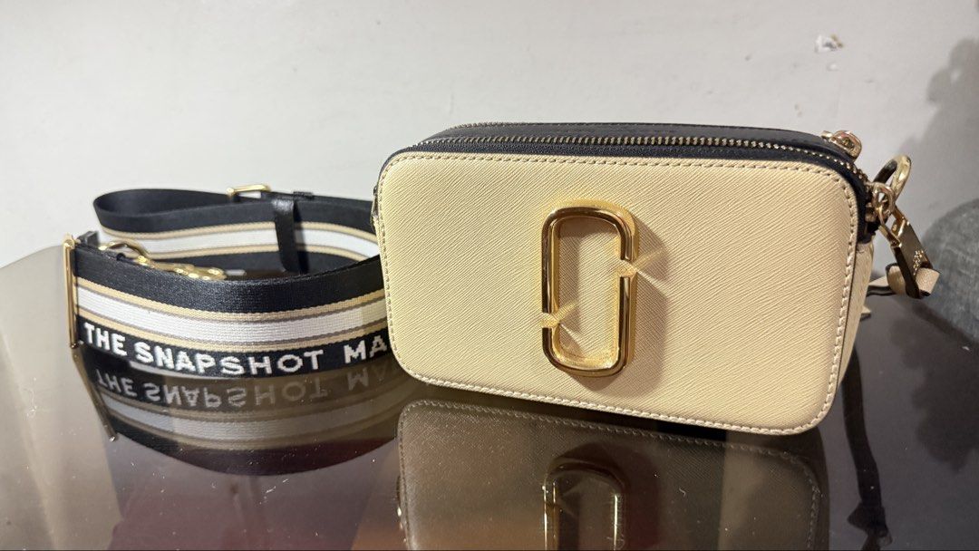 Marc Jacobs The Snapshot Camera Bag (Category: Luxury Bags & Wallets) located in San Pedro. Submitted by joe.hara (Listing ID 1440344835, Image 1). Description: - Authentic Marc Jacobs Snapshot camera bag - Chic cream and black colorway Cloud White - Signature wide strap with 'The Snapshot Marc Jacobs' branding - Polished gold hardware - Two spacious zip compartments for organization - Includes a detachable small wrist strap - Ideal for everyday 