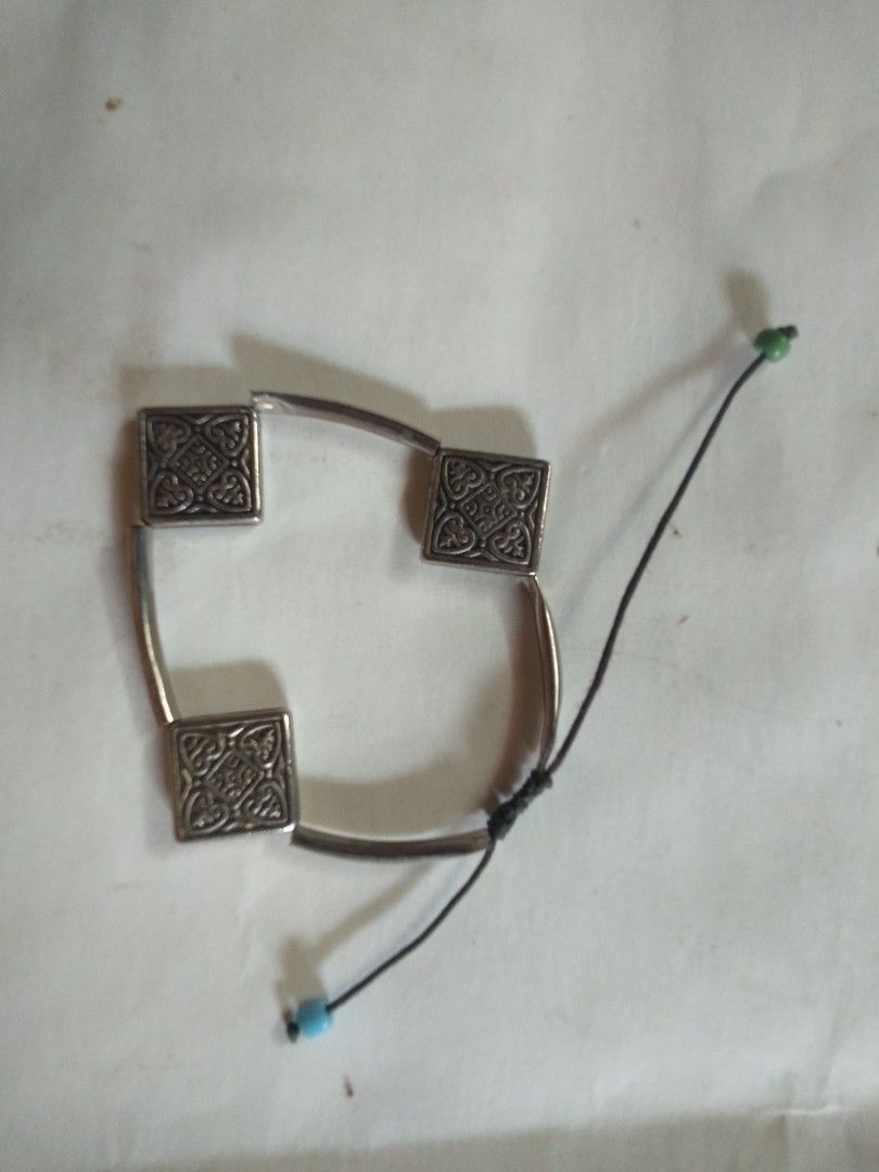 Silver Tone Bracelet with Square Ornate Charms (Category: Bracelets) located in Davao. Submitted by bravemoon_556cd5 (Listing ID 1440286435, Image 1). Description: - Silver tone bracelet - Features three square charms with intricate patterns - Adjustable cord closure with small bead accents - Unique design to add flair to your outfit.
