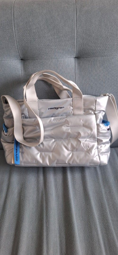 [ HEDGREN ] Silver Puffer Tote Bag with Shoulder Strap (Category: Tote Bags) located in Mandaluyong City. Submitted by crazybaggal (Listing ID 1440498430, Image 1). Description: - Hedgren silver puffer tote bag (used to be limited edition) - Shoulder strap cannot be removed - Comes with a front pouch inside that can be removed via snap closure - Red stain marks on the exterior (bottom of bag) due to proximity from another piece that was dyed red.