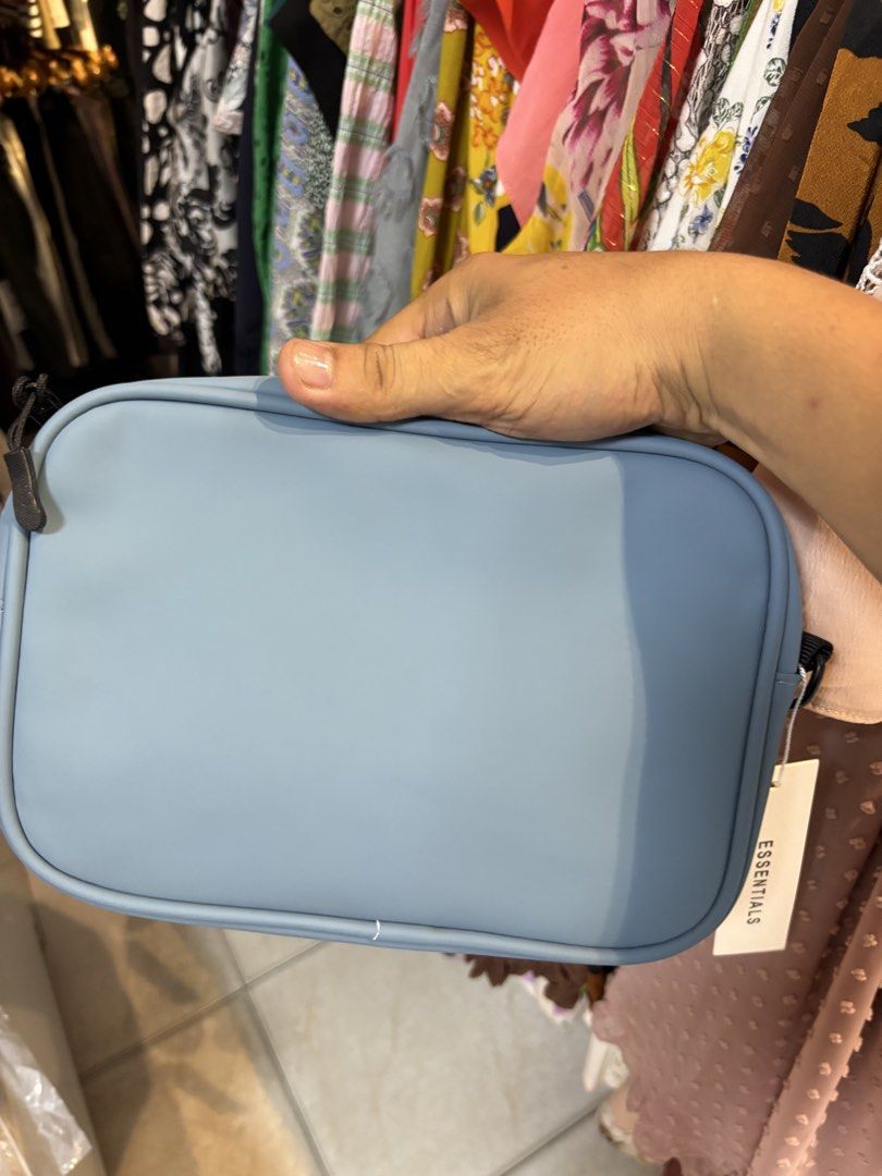 Essentials Fear of God Crossbody Bag Light Blue (Category: Luxury Bags & Wallets) located in Lopez. Submitted by thrift.ni.roms22 (Listing ID 1440511148, Image 3). Description: - Light blue crossbody bag from Essentials - Features 'ESSENTIALS' logo printed on the front - Adjustable black strap with 'ESSENTIALS' branding - Black interior - Original tag included.