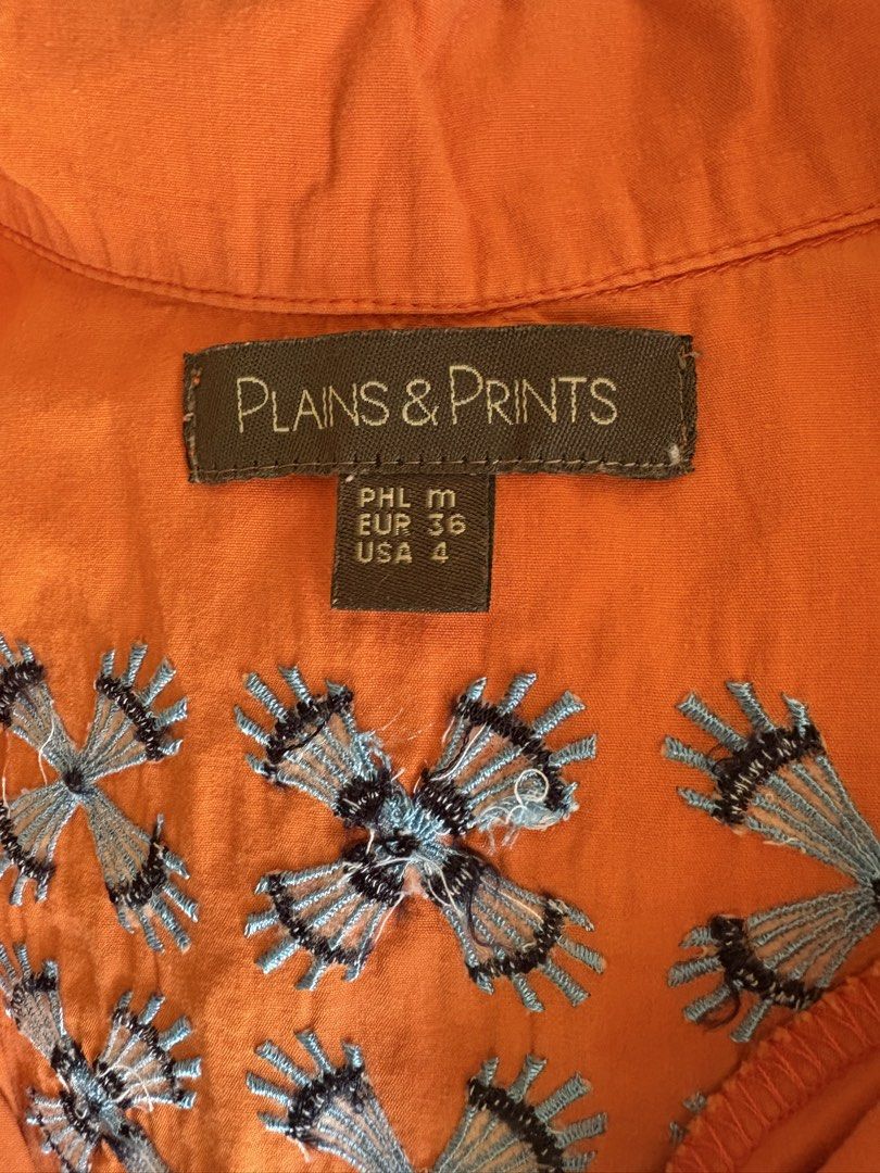 Plains & Prints Wrap Blouse (FREE SHIPPING) (Category: Blouses) located in Jaen. Submitted by relovique_finds.ph (Listing ID 1440386756, Image 3). Description: - Orange wrap blouse from Plains & Prints - Short sleeves and collared neckline - Adjustable tie waist for a flattering fit - Unique blue and grey floral embroidery on the back - Perfect for casual or dressed-up looks.